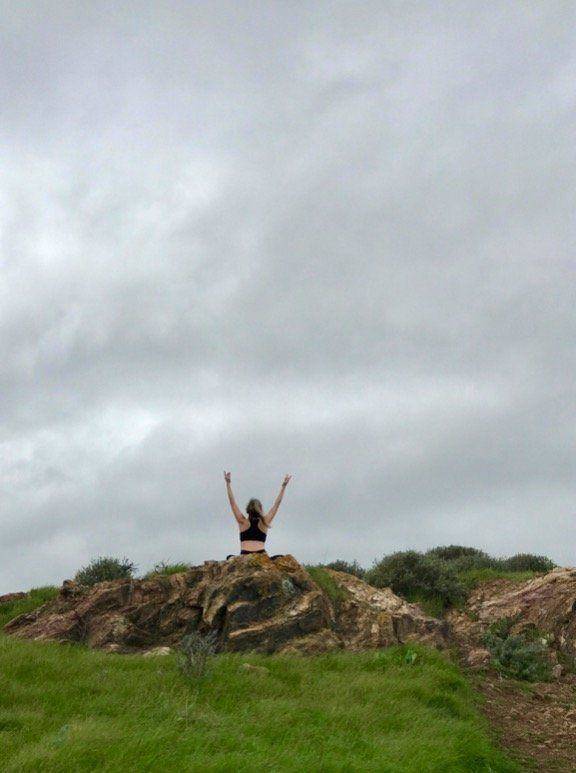 Photo of woman sitting atop a grassy hill, arms skyward