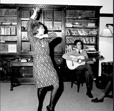 Black and white photo, probably from the 1960s or so, of the Duchess dancing with a guitarist.