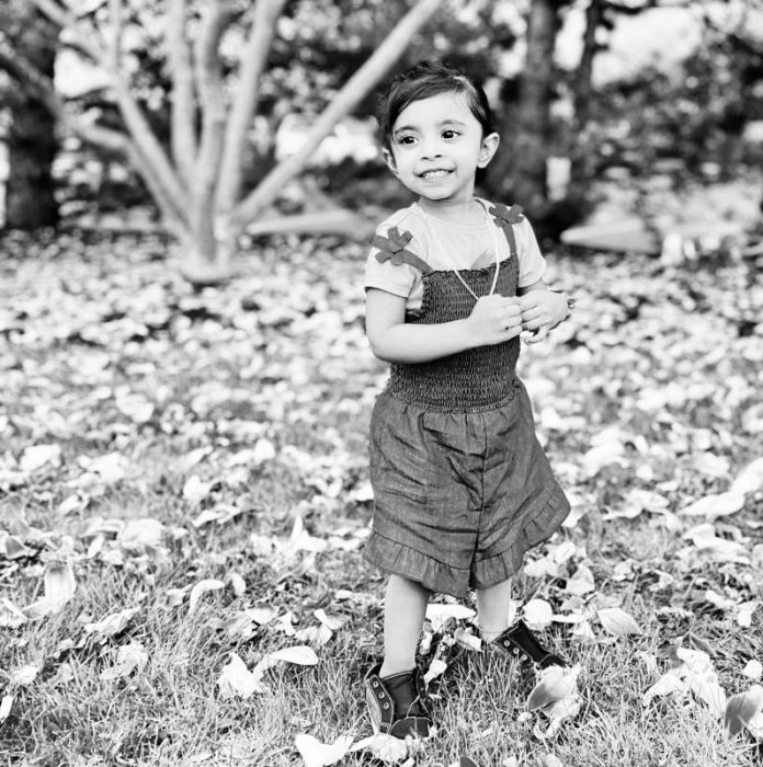 Black and white photo Vedha's daughter standing in a grassy field. 