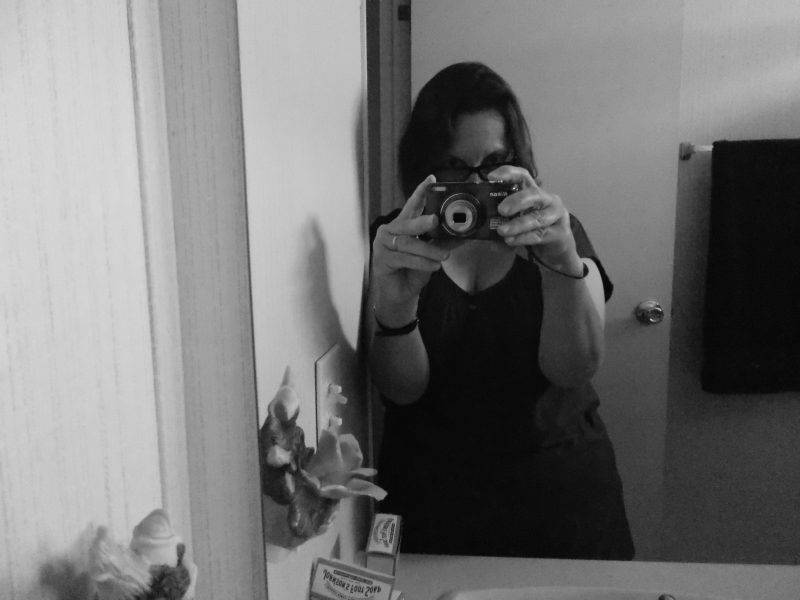 Black and white photo of writer Dawn Pisturino taking a selfie in front of a mirror, her face covered by the camera.