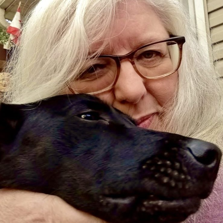 Photo of Debbie D. hugging a black dog.