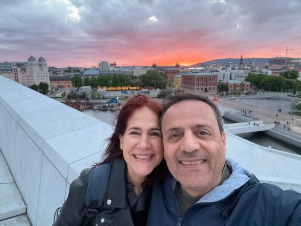da-AL and Khashayar smiling on the balcony of the Oslo Opera House, a pink sunset behind them.
