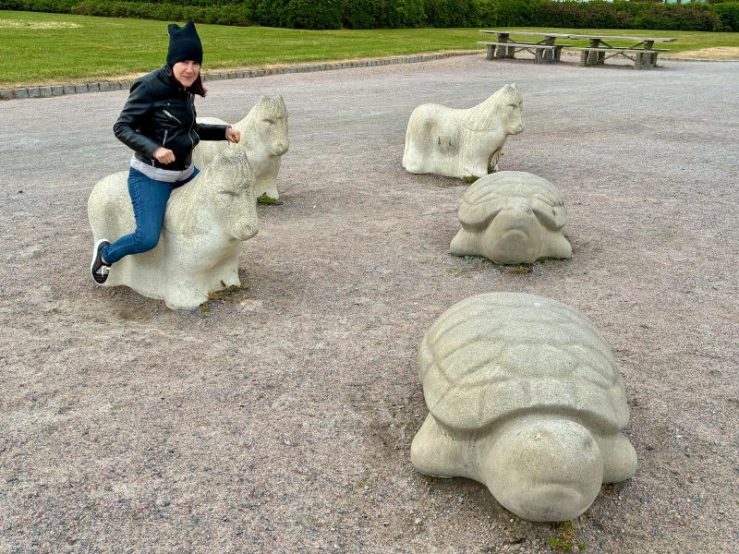 da-AL riding a big sculpture sea animal among several others  that include turtles at a park area.