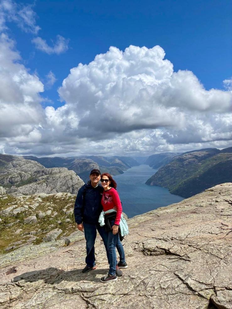 Man and woman standing on the flat, massive cliff of Preikestolen, overlooking a dramatic fjord.
