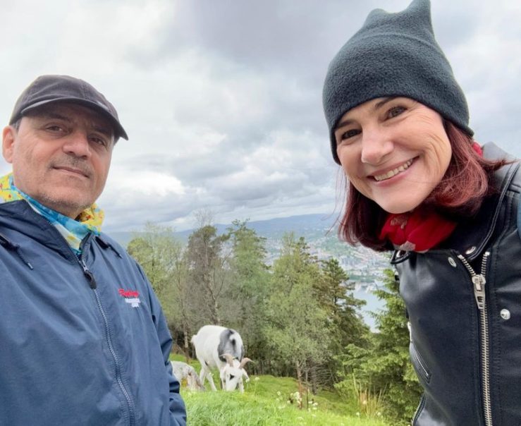 Photo of Khashayar and da-AL at the top of a hill overlooking Bergen, Norway. A goat is grazing in the background.